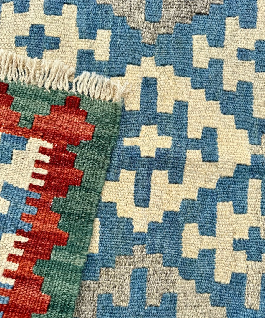 Close-up of kilim rug weave: blue, cream, and red motifs on green ground with fringe
