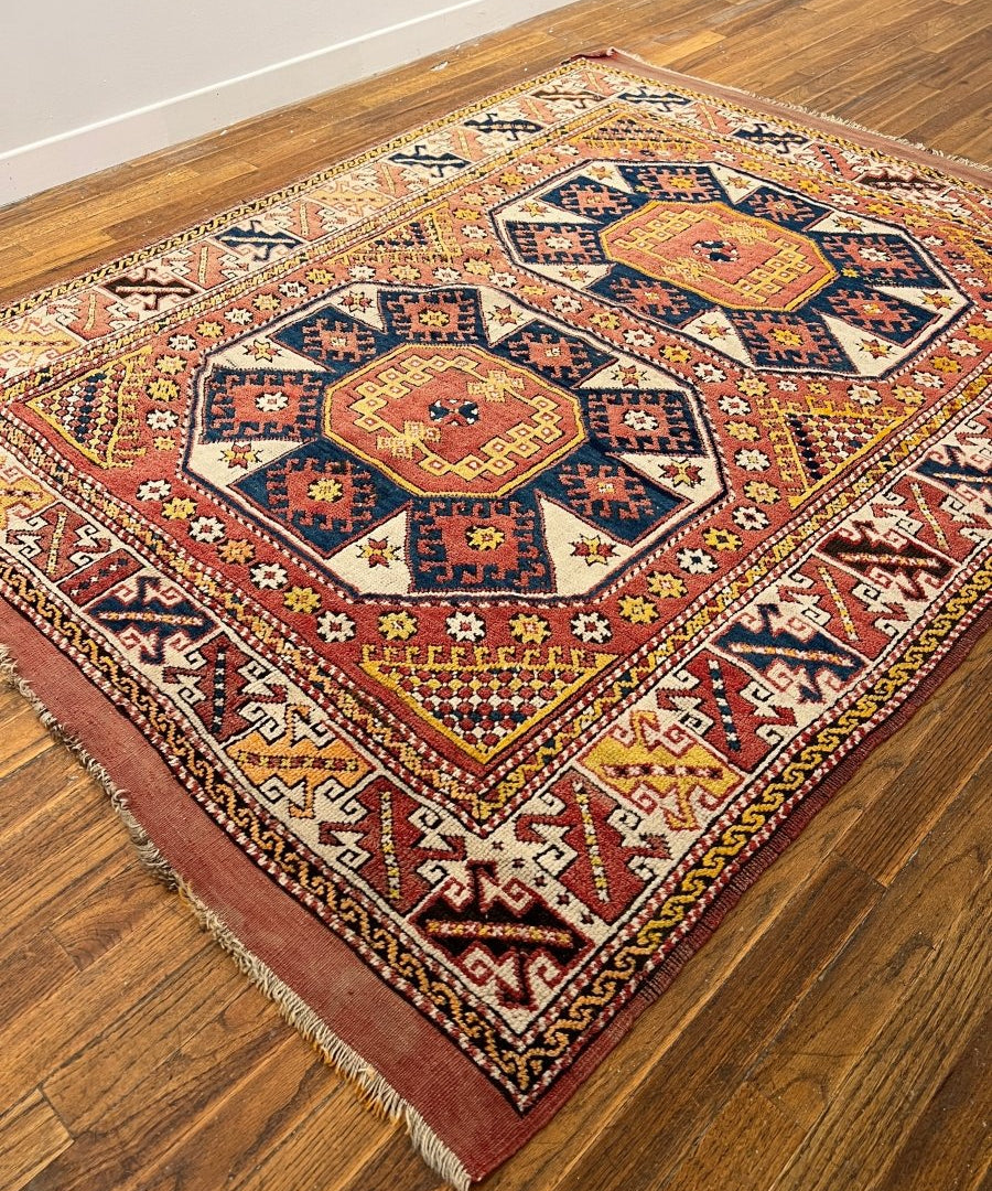 Turkish Ezine rug with red, blue, and cream geometric medallion pattern and fringed corners.