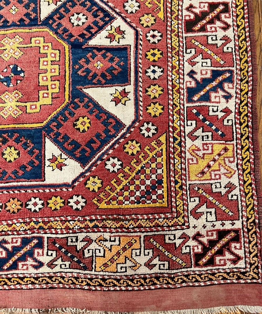 Ezine rug corner close-up with red, blue, and cream geometric motifs and detailed border.