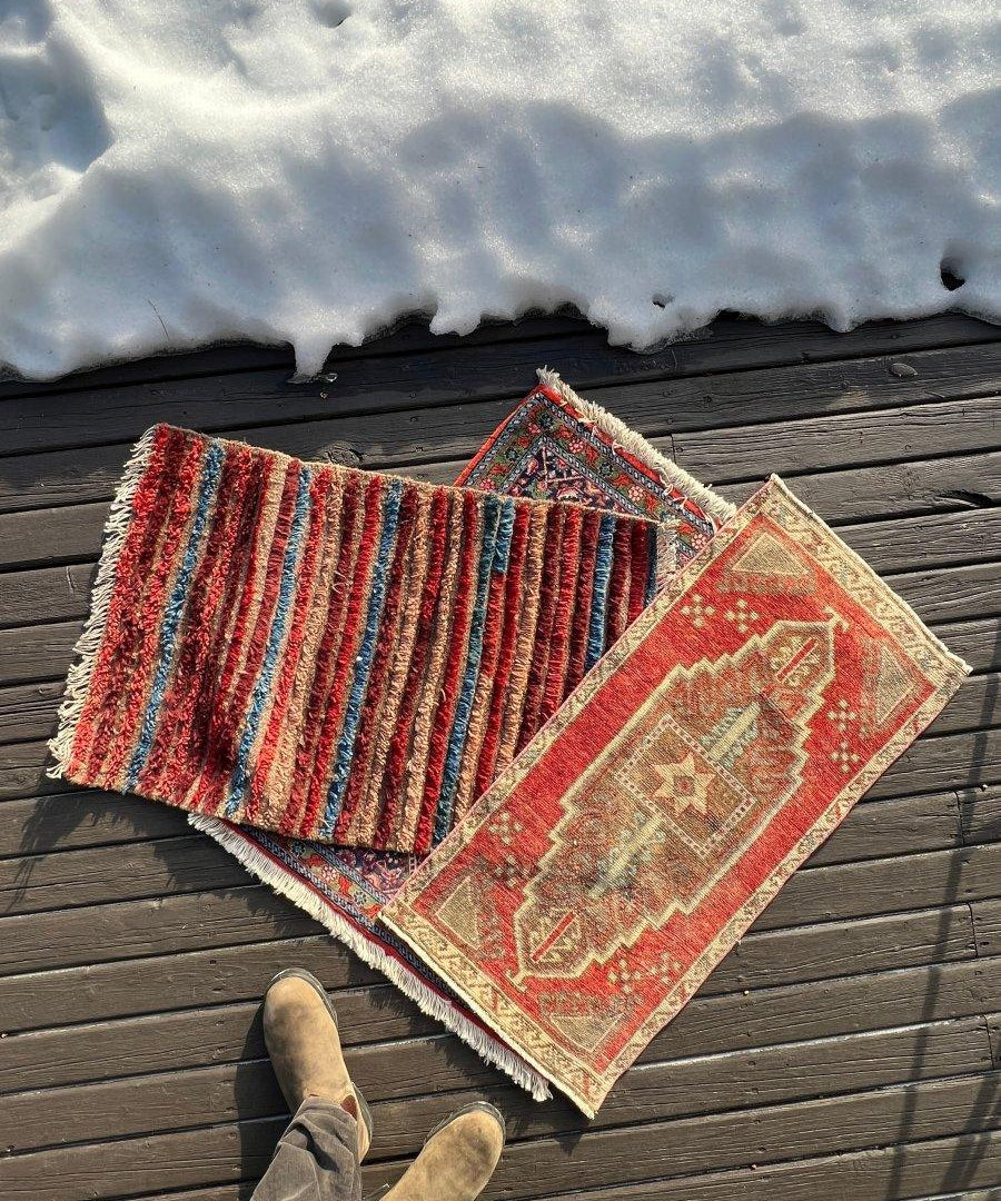 Turkish mini rugs set on wooden deck; red, teal, and striped designs with fringed borders.