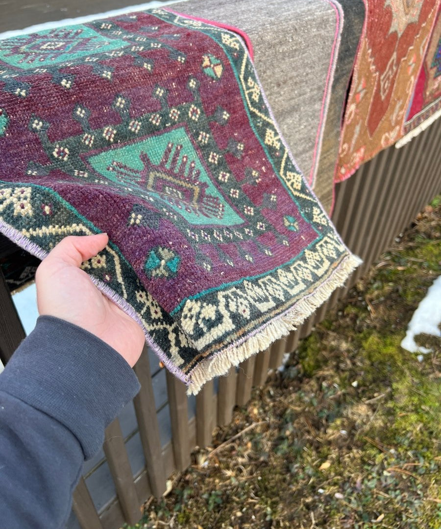 Turquoise and burgundy rug corner with patterned diamond motifs and cream fringe edging