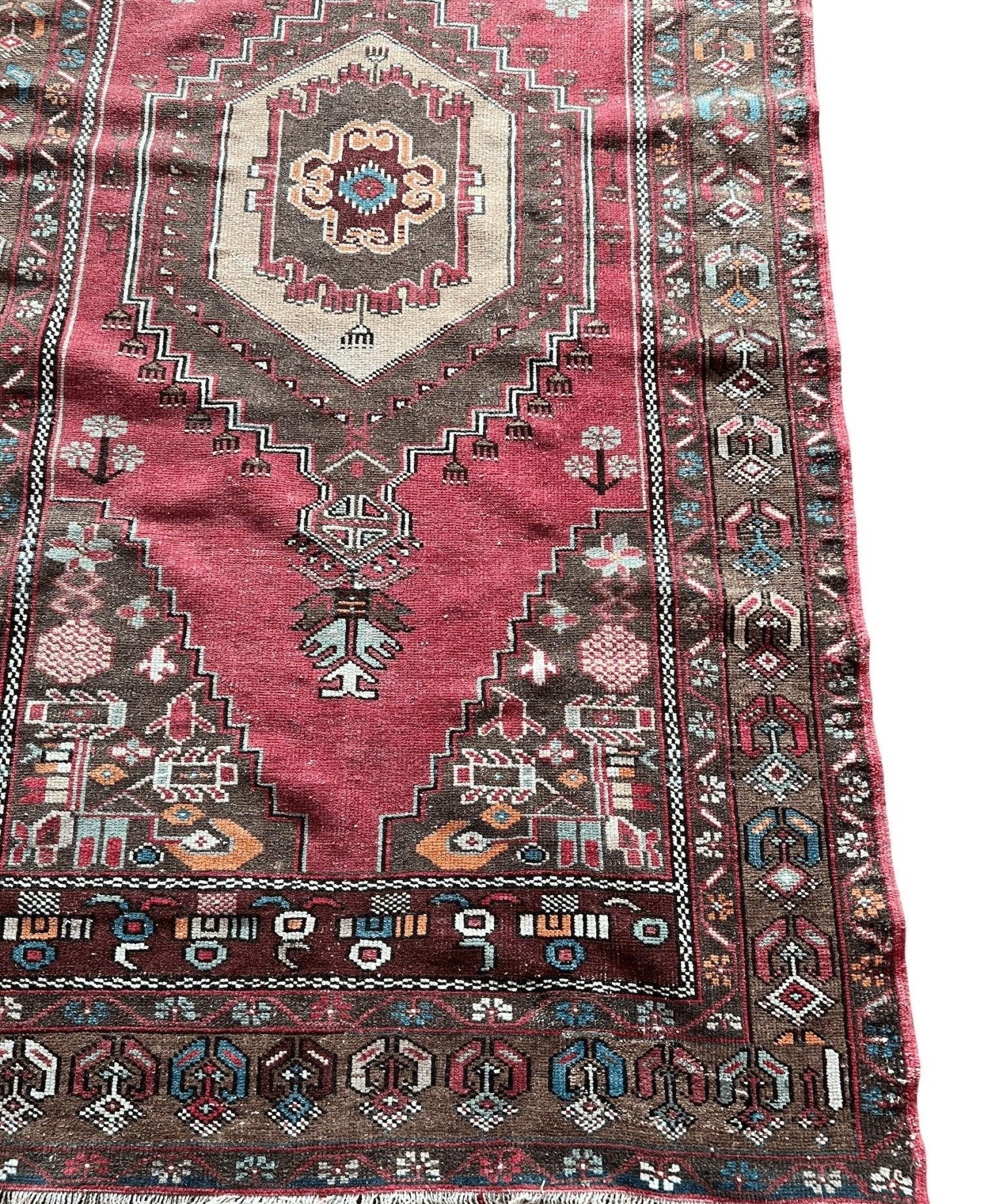 Red area rug detail with central medallion, patterned border, and visible fringe