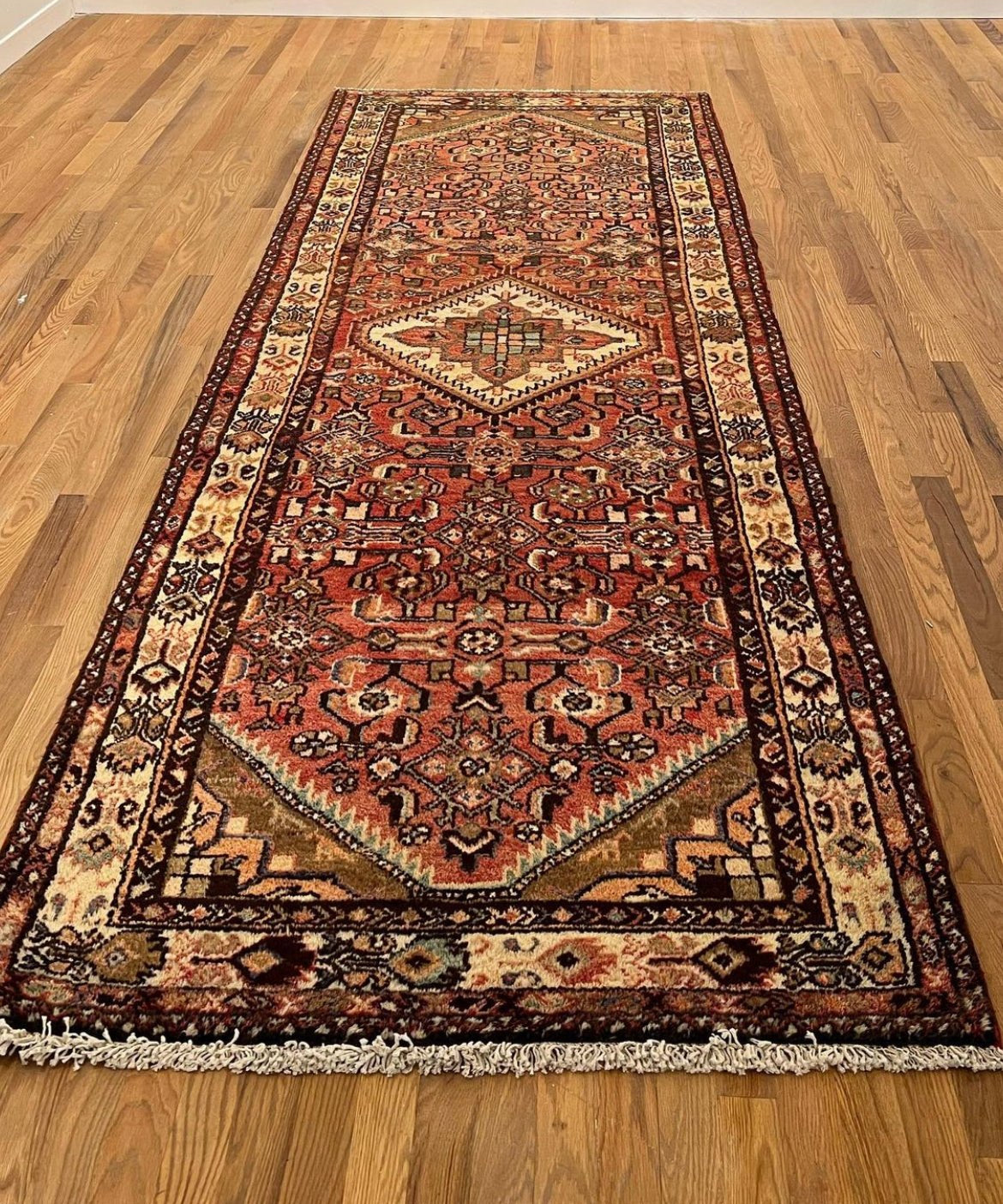 Vintage runner rug with red and beige geometric motifs, fringe along one edge