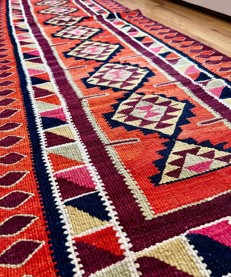 Section of tribal runner rug with red background, cream stripe, and repeating diamond shapes