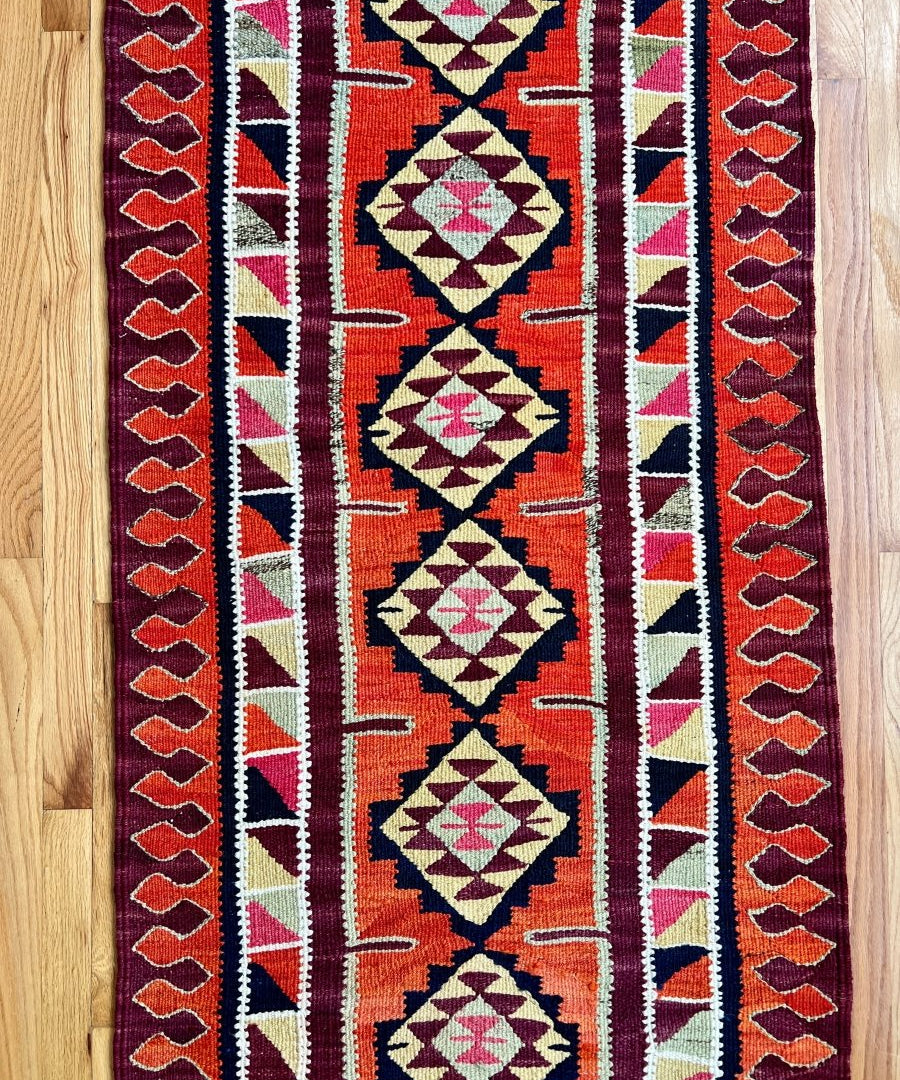 Close-up tribal runner rug pattern in red, cream, navy, and purple with diamond motifs