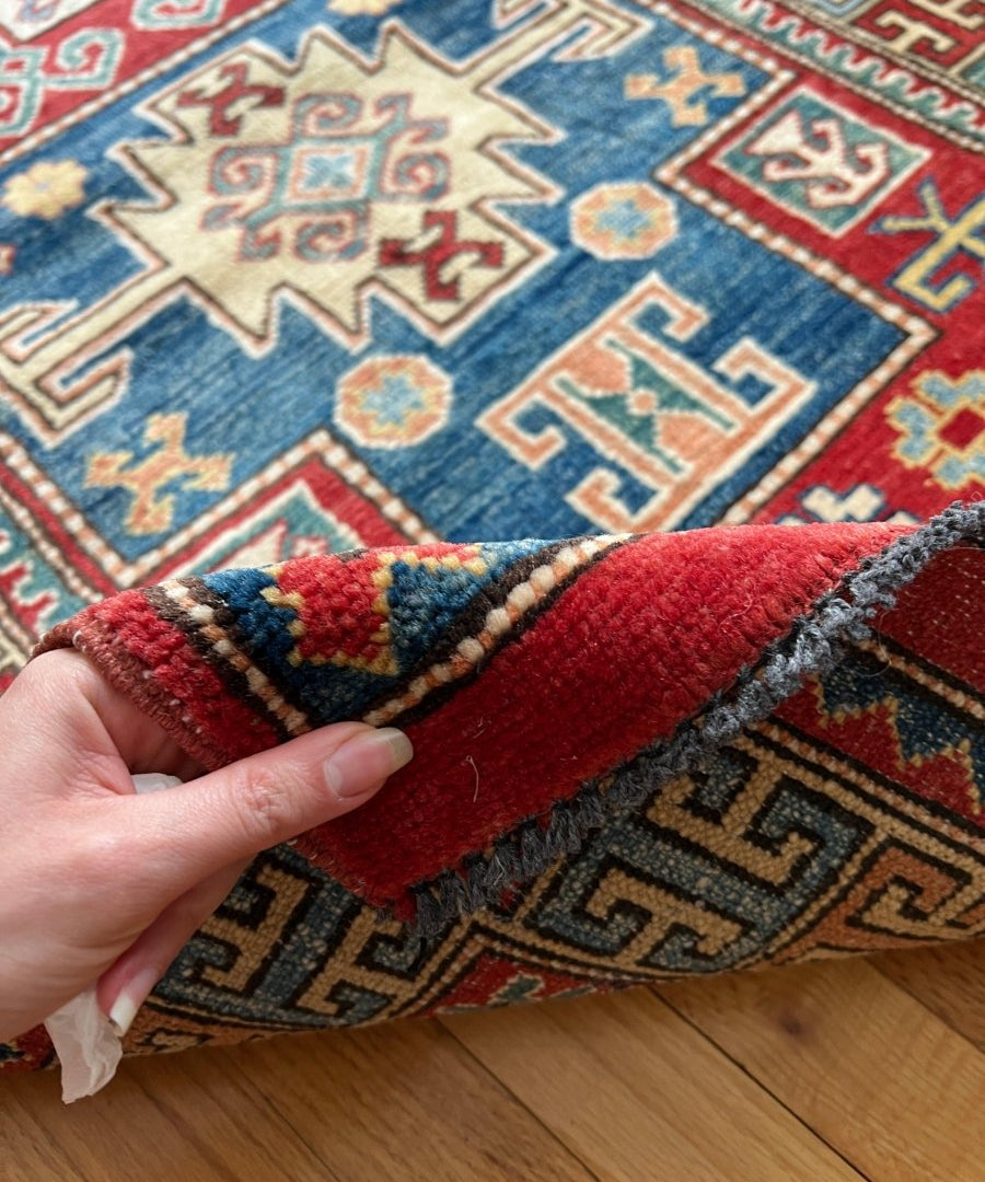 Kazak runner rug corner close-up with red fringe and multicolor geometric motifs