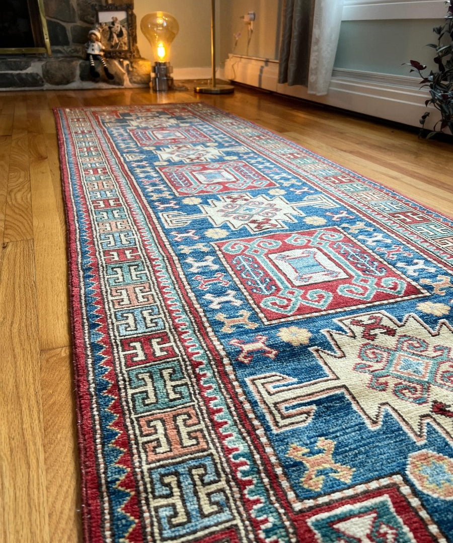 Kazak rug runner with blue geometric pattern and red trim, laid on wood floor